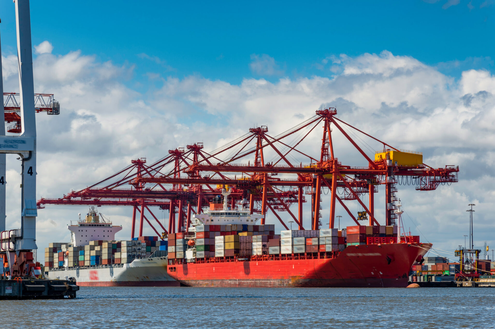 Large red container ship docked at a harbor next to tall red cranes