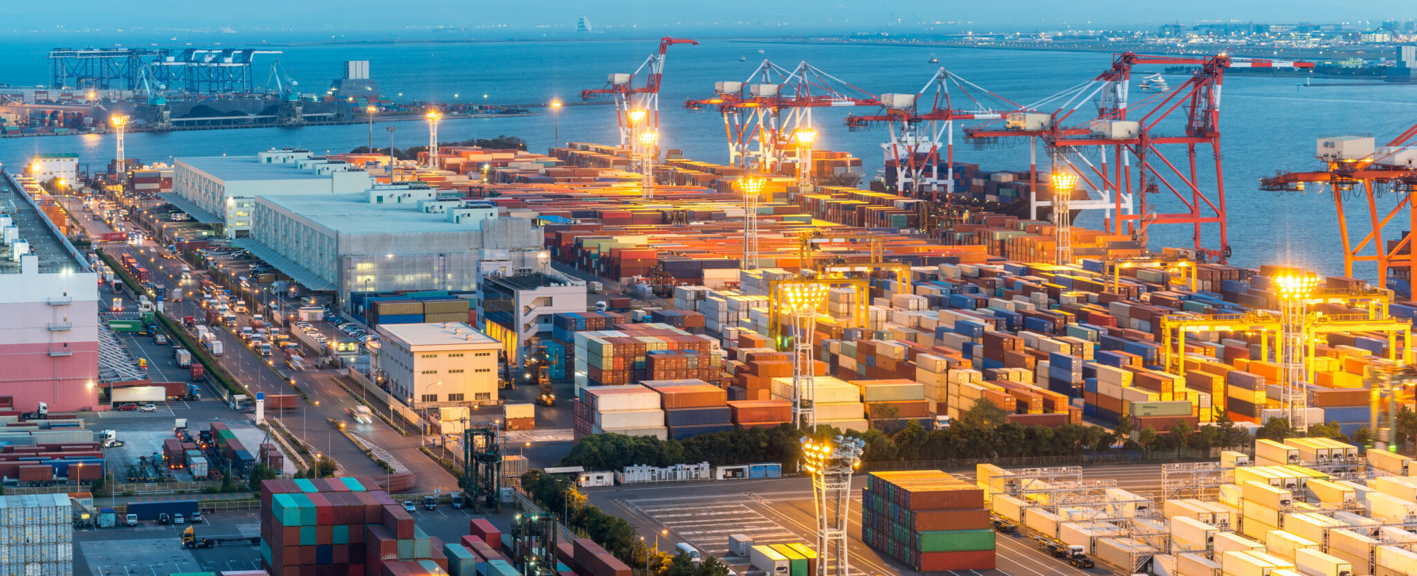 Panorama showing colorful shipping containers are stacked along the coast beneath red and white cranes
