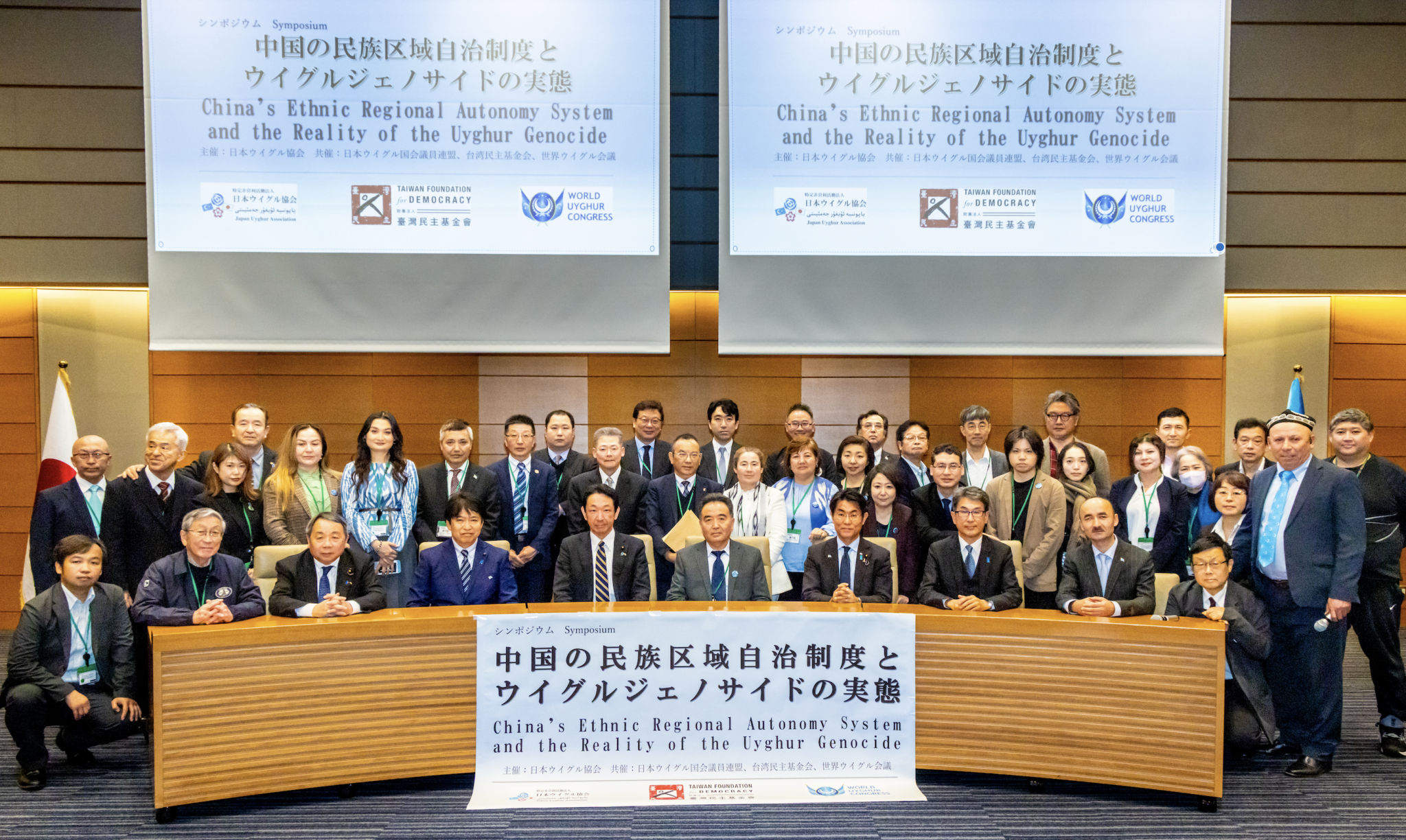 Roughly fourty people in suits gathered behind a large wooden dais.