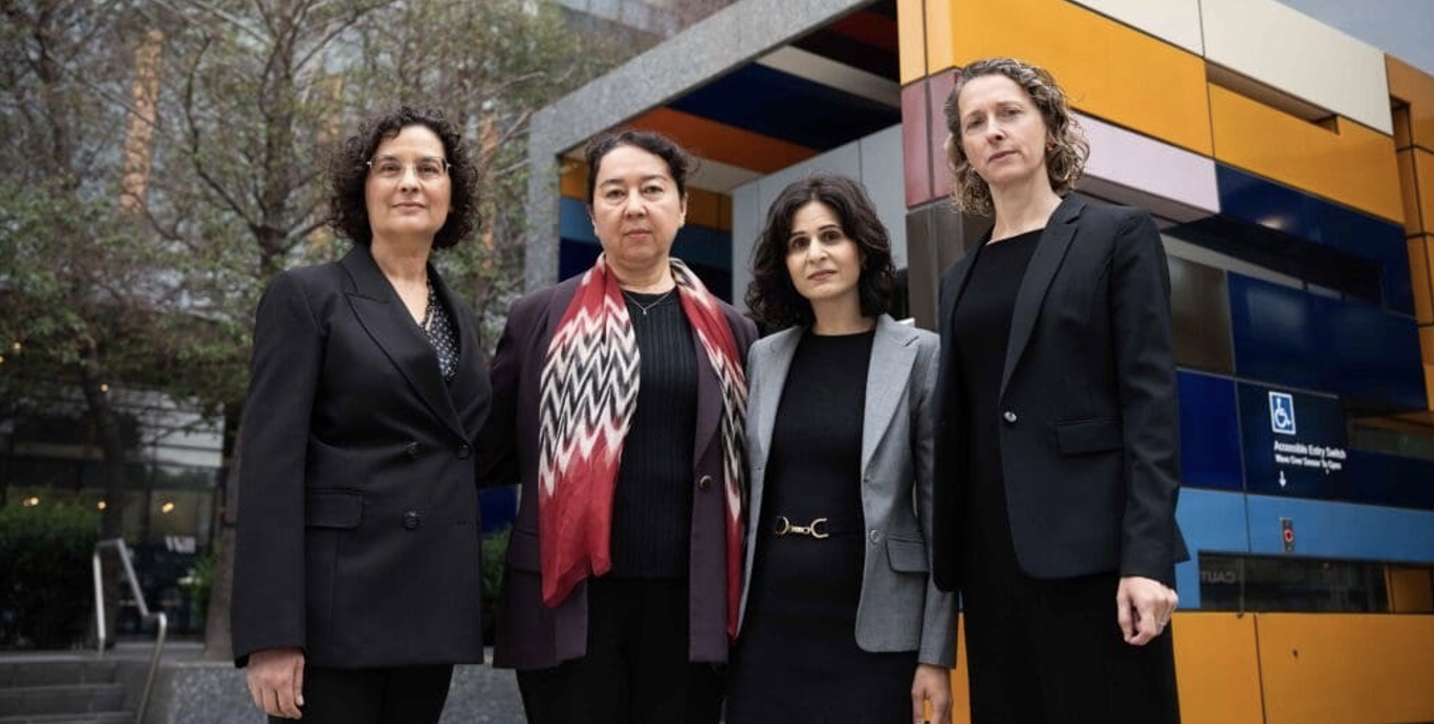 Four women in dark suits stand outside in front of a colorful office building